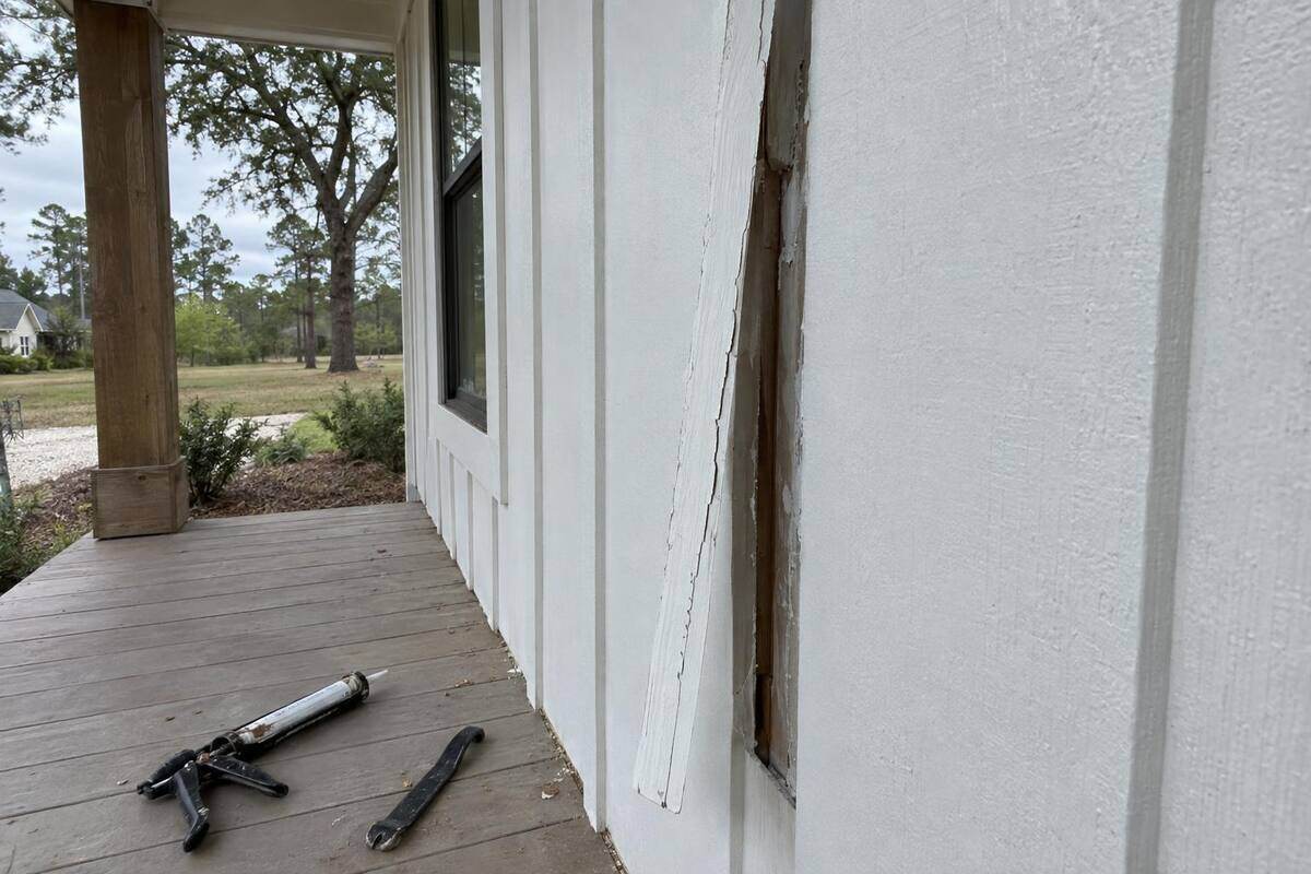 White vertical siding beside a porch post with one batten strip pulled loose and cracked paint