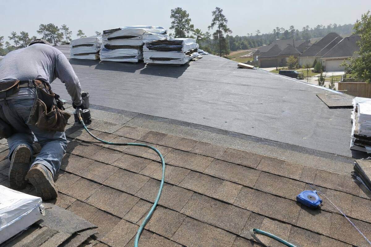 Roofer laying a new course of shingles over fresh underlayment with bundles stacked near the ridge