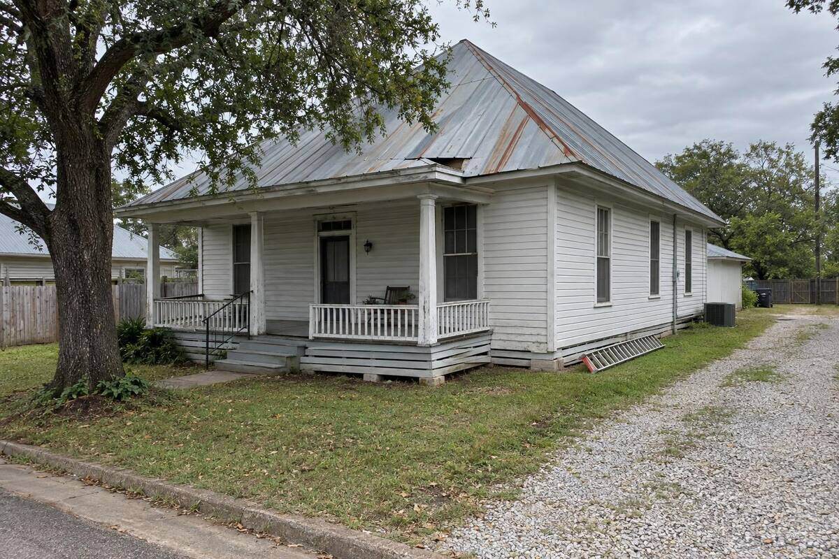 Early wood-frame house with a front porch and an aged metal roof with rust streaks