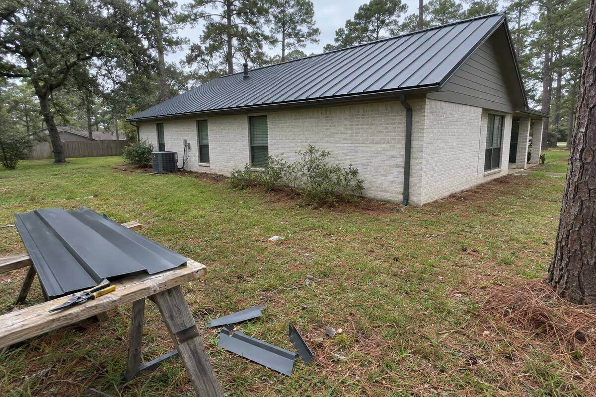 One-story house with a charcoal standing-seam metal roof and panel offcuts on a sawhorse in the side yard